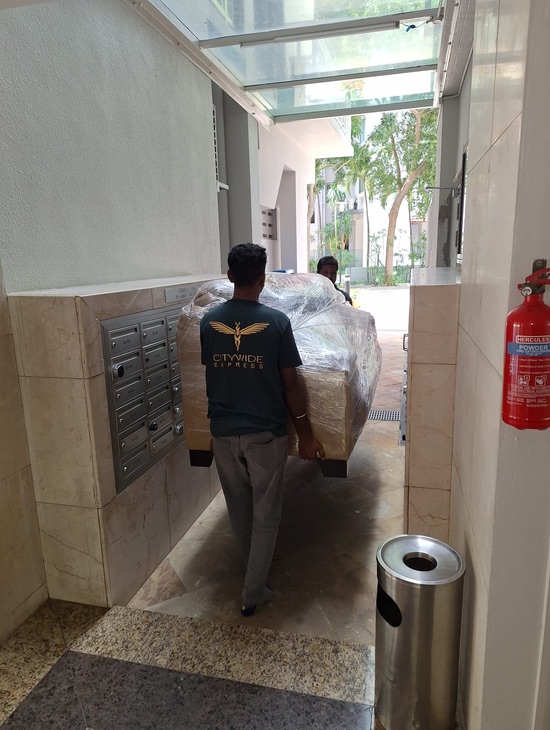 Two Citywide Express employees providing furniture moving service by carrying a shrink wrapped sofa through the gallery