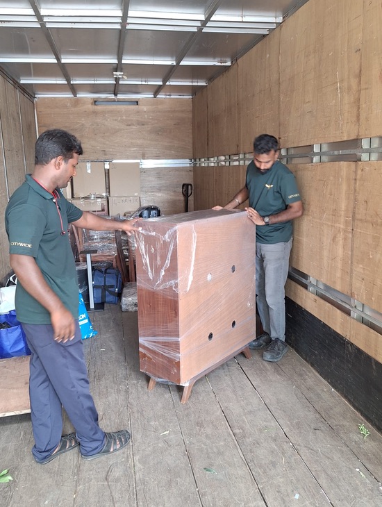 Two Citywide Express employees moving a shrink wrapped medium sized almirah in the lorry