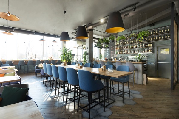 A restaurant setup featuring a long table, blue chairs, and a front bar, adorned with green trees