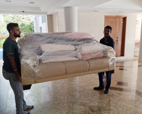 Two Citywide employees providing furniture moving service by carrying a shrink wrapped sofa